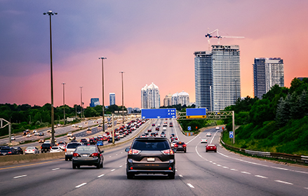 Vehicles running on unleaded fuel driving down multi-lane Canadian highway at sunset.